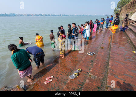 Il Dakshineswar Kali Temple Ghat sulle rive del Fiume Hooghly con la popolazione locale la balneazione e lavaggio in una giornata di sole con cielo blu. Foto Stock