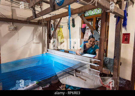 Un locale donna indiana che lavora con un tradizionale handloom rendendo il materiale di seta per un saree nel suo piccolo negozio. Foto Stock