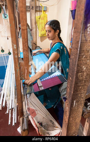 Un locale donna indiana che lavora con un tradizionale handloom rendendo il materiale di seta per un saree nel suo piccolo negozio. Foto Stock