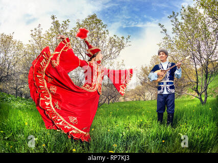 Il kazako woman dancing in abito rosso e uomo dombra giocando a fioritura primaverile giardino ad Almaty in Kazakistan e in Asia centrale Foto Stock