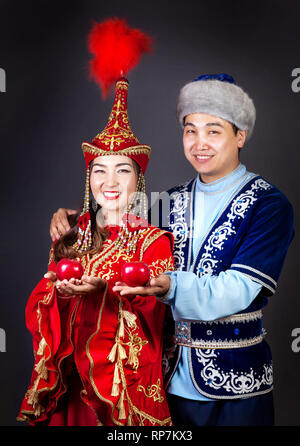 Coppia asiatica in nazionale costumi kazako tenendo le mele rosse a sfondo grigio Foto Stock