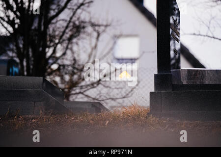 Il Menorah bokeh silhouette nella finestra di una casa vicino al soggetto ad atti vandalici tombe con simboli nazisti in blu spray-dipinte sulle tombe danneggiato - Cimitero Ebraico in Quatzenheim vicino a Strasburgo . Foto Stock