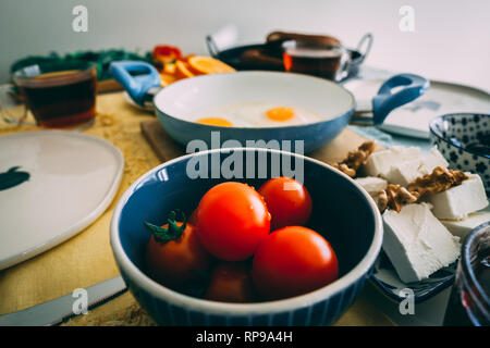 Chiudi immagine di pomodori serviti per colazione. Tpmatoes nella ciotola sul tavolo con altri piatti in background. Foto Stock