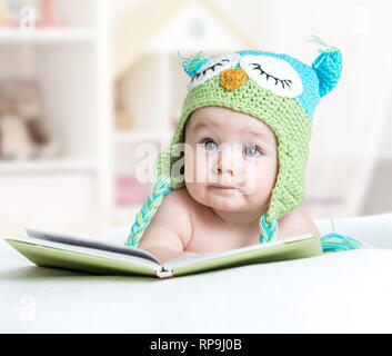 Baby infany in funny owl berretto lavorato a maglia gufo giacente con libro in vivaio Foto Stock