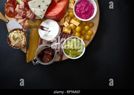 Scheda di antipasti con vari formaggi e carni spuntini con hummus e olive sulla rotonda di legno sul bordo tavola nera Foto Stock