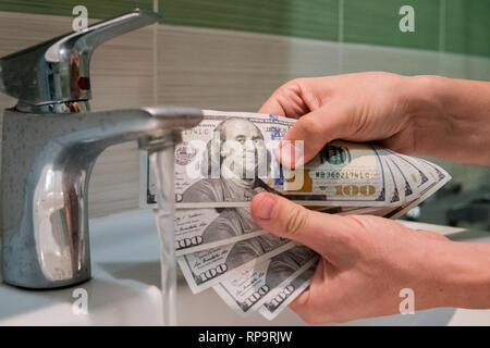 Concetto di riciclaggio di denaro. Le banconote di 100 di dollari nelle mani di uomini vicino a getti d'acqua nel lavandino. Foto Stock