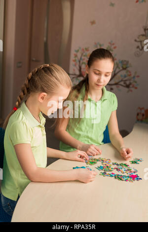 Due bambine risolvendo puzzle insieme seduti a tavola Foto Stock