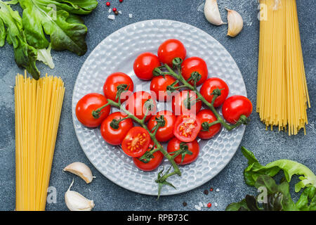 Materie pasta italiana spaghetti e cottura Ingredienti pomodorini verdi. Il cibo italiano pietra scura sullo sfondo. Vista da sopra con copia spazio. Foto Stock