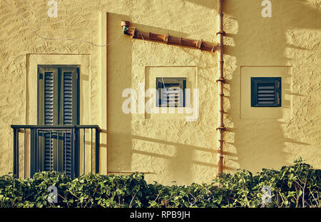Giallo a parete resistente con persiane e ceramica vecchia grondaia, dai toni di colore dell'immagine. Foto Stock