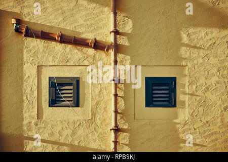 Giallo a parete resistente con persiane e ceramica vecchia grondaia, dai toni di colore dell'immagine. Foto Stock