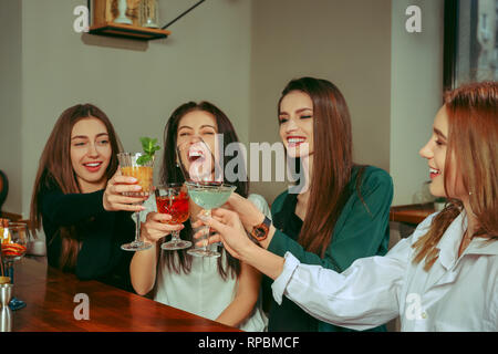 Amici di sesso femminile avente un drink al bar. Essi sono qui seduti a un tavolo di legno con cocktail. Essi sono bicchieri tintinnanti Foto Stock