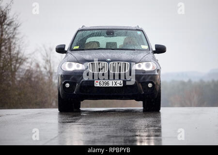 GRODNO, Bielorussia - Ottobre 2016: BMW X5 vista frontale con luci incandescenti in piedi su asfalto umido sotto la pioggia coperti con gocce di pioggia su grigio piovoso sk Foto Stock