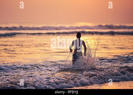 Vacanze sulla spiaggia. Felice giovane uomo che corre verso il mare al tramonto. Foto Stock