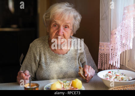 Donna anziana mangia seduto al tavolo. Foto Stock