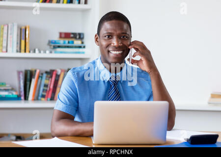 Ridendo African American imprenditore con cravatta al telefono cellulare in ufficio Foto Stock