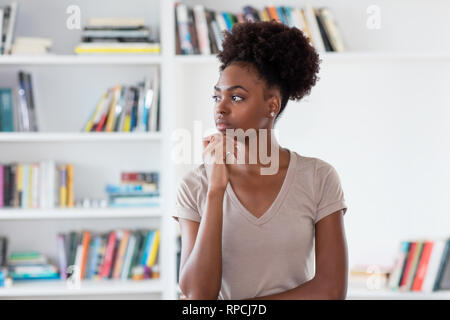 Il pensiero americano africano giovane donna adulta in interni a casa Foto Stock