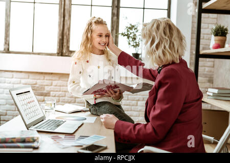 Sorridente bambino allegro tenendo la bellezza magazine mentre madre toccando il suo volto Foto Stock