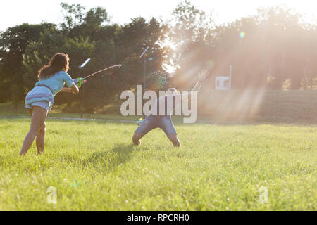 Un giocoso coppia giovane che si rincorrono e giocando con le pistole di acqua in un prato ar tramonto. Foto Stock