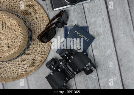 Concetto di viaggio con la mens cappello di paglia 2 passaporti binocolo occhiali da sole e una macchina fotografica su un alterato grigio Sfondo legno Foto Stock