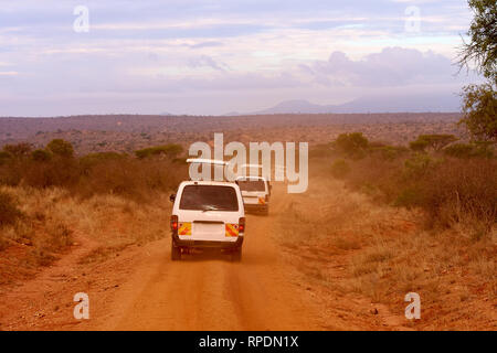 Numerose vetture di safari in Kenya in Africa, sabbia rossa e montagne sullo sfondo Foto Stock