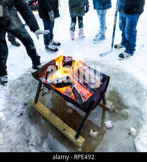 Le persone in fase di riscaldamento intorno al fuoco all'aperto pit, indossando pattini da ghiaccio a forche, Winnipeg, Manitoba, Canada. Foto Stock