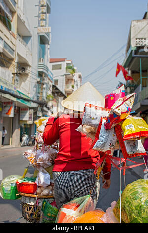 Una femmina di commerciante vietnamita porta i suoi prodotti lungo la strada. Foto Stock