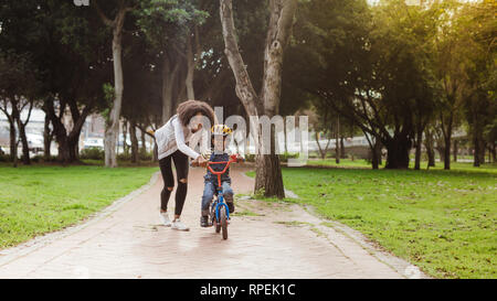 Piccolo ragazzo di età prescolare e sua madre nel parco con una bicicletta. Madre insegnamento suo figlio in bicicletta al parco. Foto Stock