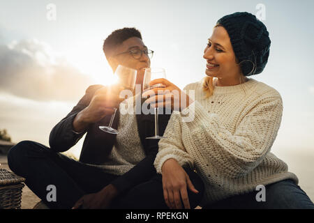 Coppia giovane di bere vino e godendo di un picnic. Coppia adorabile tostare vino seduti all'aperto sulla giornata di sole. Foto Stock