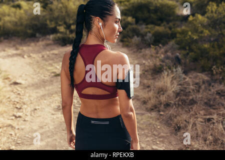 Runner in sportswear permanente sulla croce il percorso del paese. Femmina su sentiero di montagna in mattina, pronto per l'esecuzione di allenamento che guarda lontano. Foto Stock