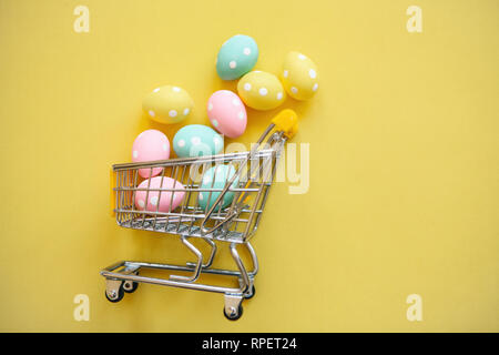 Carrello con uova su uno sfondo giallo. Il concetto di una festa di Pasqua in vendita in stile minimale. Foto Stock