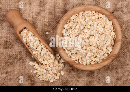 Fiocchi di avena in una ciotola di legno con un convogliatore su un letto di sacco Foto Stock