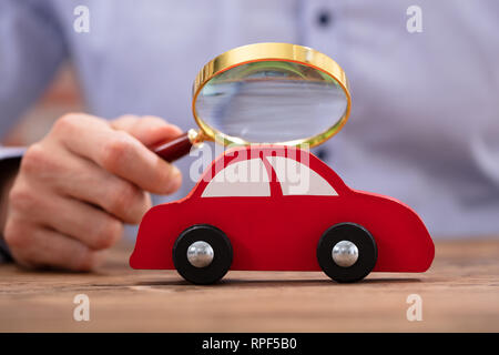 Close-up di una persona della mano che tiene la lente di ingrandimento cercando Red giocattolo auto Foto Stock