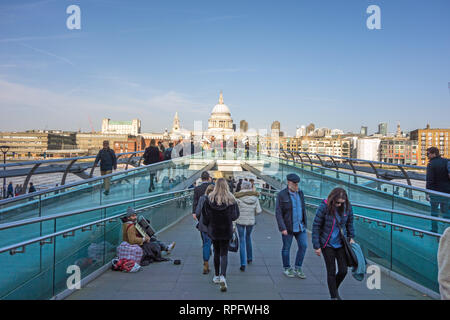 Uomini donne gente camminare sopra il Millennium bridge verso la Cattedrale di St Paul che attraversano il fiume Tamigi Londra Inghilterra con il blu del cielo Foto Stock