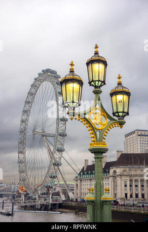 Palo per lampada in ghisa a tre teste ornato con luci a gas accese sul Westminster Bridge, Inghilterra, Londra, con l'occhio di Londra sullo sfondo Foto Stock