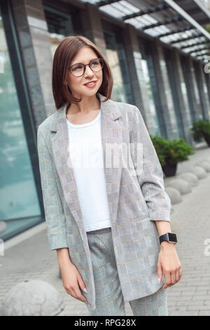 Business casual. Signora giovane in occhiali camminando sulla strada di città sorridendo felice Foto Stock