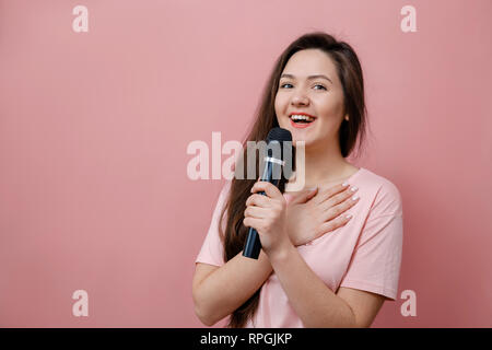 Giovane donna smilling con microfono in mano su sfondo rosa Foto Stock