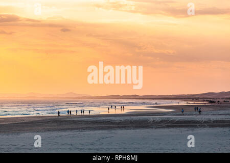 Le persone che si godono il bel tempo sulla spiaggia dell'oceano al tramonto Foto Stock