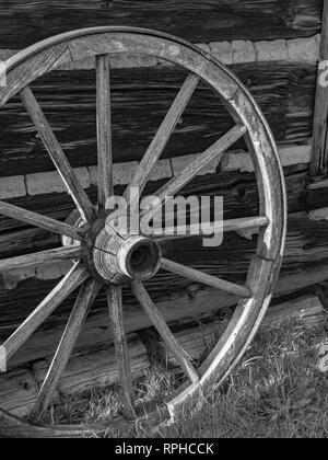 Weathered antichi ruota di carro appoggiata contro un vecchio fienile con split log e spiraglio di costruzione. Foto Stock