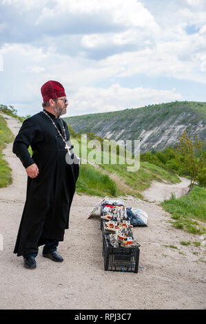 Un sacerdote la vendita soprammobili per i turisti al di fuori del Orhei Vechi Grotta monastero in Moldavia. Foto Stock