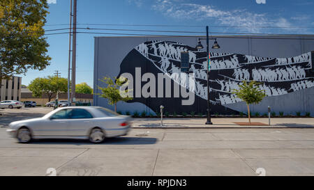 Street murale dipinto principalmente in bianco e nero che mostra una testa di donna con un grigio auto passando da con motion blur a Sacramento, California Foto Stock