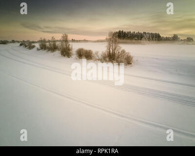 Le motoslitte hanno lasciato tracce sul fiume di ghiaccio su un freddo inverno pomeriggio al nord della Finlandia. La nebbia sale dalla congelati campi, quando il Foto Stock