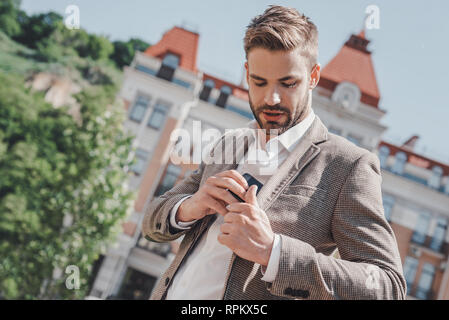 Bel giovane imprenditore mette il telefono nella sua tasca della giacca a camminare su una strada di città di mattina andando a lavorare in ufficio wear casual elegante vestito di giacca marrone e camicia bianca. Uno stile di vita urbano di giovani professionisti. Foto Stock