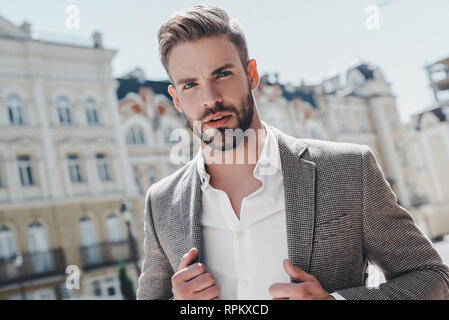 Bel giovane imprenditore camminando sulla strada della citta'. Egli è di andare a lavorare in ufficio wear casual elegante vestito di giacca marrone e camicia bianca. Uno stile di vita urbano di giovani professionisti. Foto Stock