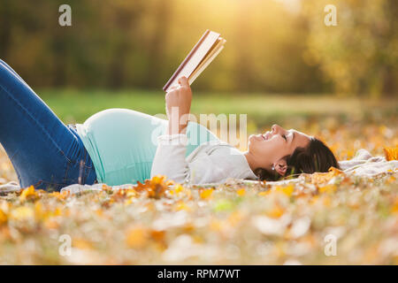 Donna incinta relax nel parco. Ella è la lettura del libro. Foto Stock