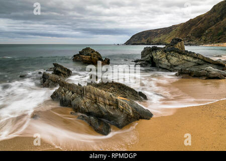Si tratta di una lunga esposizione fotografia di onde in movimento attraverso le rocce su una spiaggia di sabbia. Questa è stata presa su Kinnago nella Baia di Donegal Irlanda Foto Stock