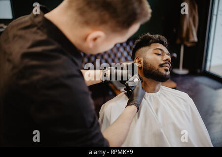 Chiudere l'uomo con la barba client in Barberia parrucchiere barbiere sulla rasatura rasoio elettrico Foto Stock