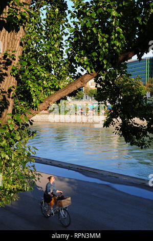 Giovane donna su una bicicletta lungo il Donaukanal, Vienna, Austria. In background, Herrmann Strandbar, Vienna spiaggia urbana Foto Stock