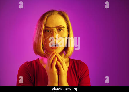 Il motivo è che. Bellissima femmina di metà lunghezza ritratto isolato sul trendy neon pink studio backgroud. Giovani sorpreso emotivo, frustrato e disorientati donna. Le emozioni umane, espressione facciale concetto. Foto Stock