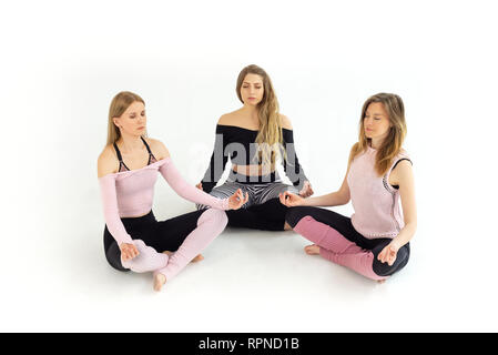 Un gruppo di giovani belle ragazze da tre persone fare yoga zen, meditazione con gli occhi chiusi. Sfondo bianco Foto Stock