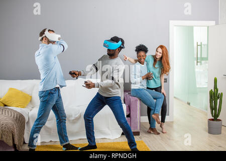 Gruppo di multirazziale maschio femmina amd gli studenti la riproduzione di gioco virtuale utilizzando occhiali VR, divertirsi insieme ay home - Virtual omg la realtà e portatile di Foto Stock